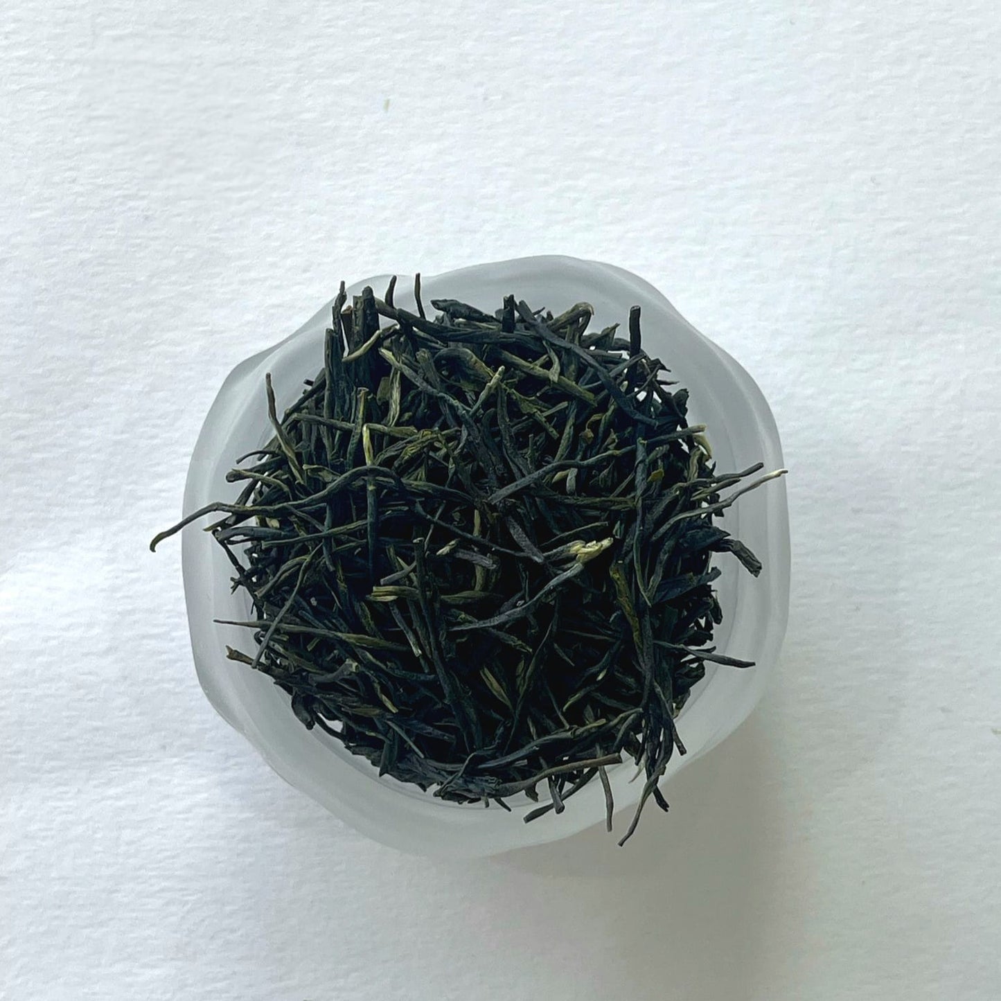 Dry green tea leaves in a clear glass container on a white background