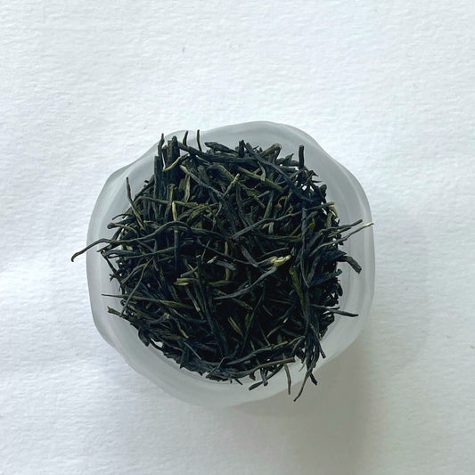 Dry green tea leaves in a clear glass container on a white background