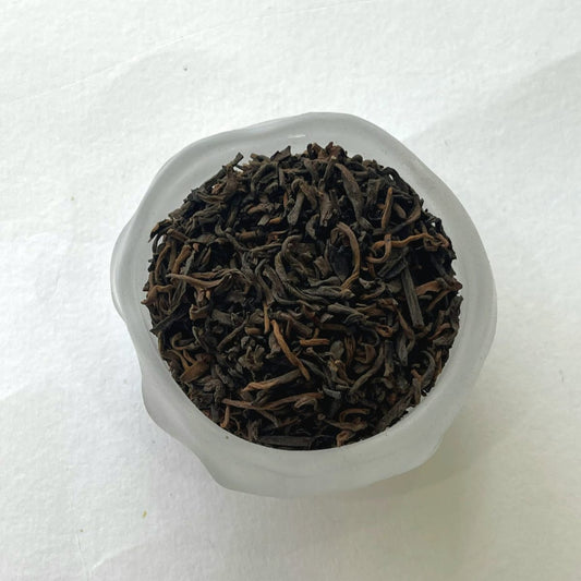 Dry brown tea leaves in a clear glass container on a white background
